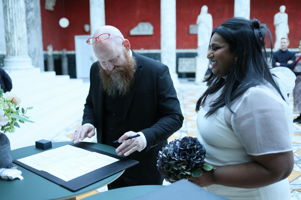 A couple signing marriage documents with a bouquet