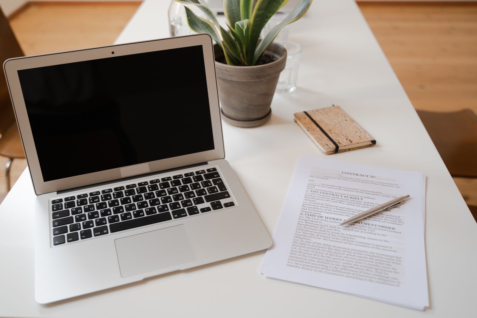 A desk with a laptop, a plant and a contract