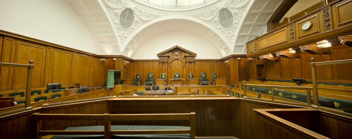 Empty courtroom featuring rich wooden paneling and a decorative ceiling