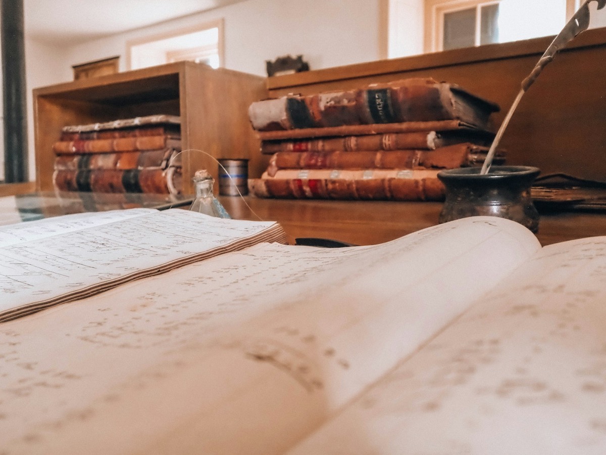 Open book, old books, and a quill on a desk