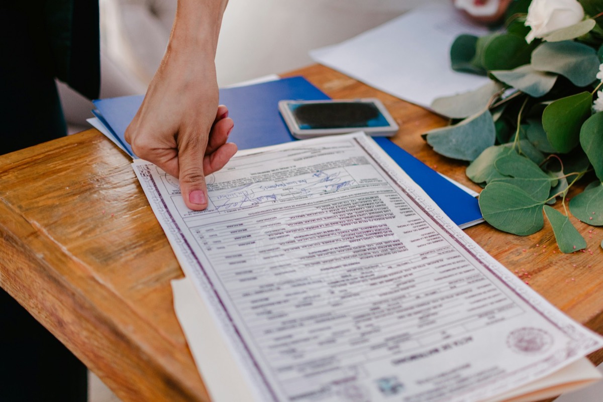 Person pointing at a marriage certificate on a wooden table